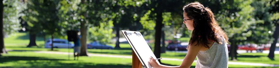 Female Student Drawing on Art Easel on Campus Front Lawn